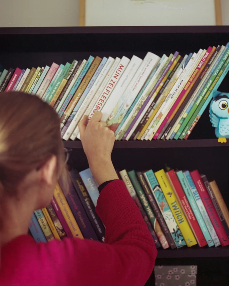 Laura pakt een boek uit haar kast vol Nederlandse kinderboeken